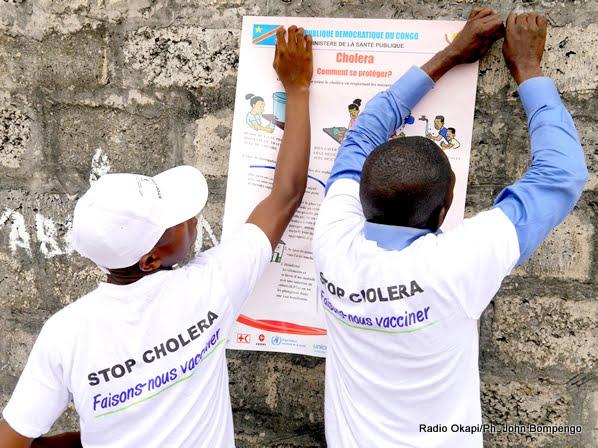 Zone de Pakadjuma, Province de Kinshasa, RD Congo: Des mobilisateurs sociaux mettent en place des affiches sur les mesures-clés pour éviter le choléra dans la zone de santé de Pakadjuma touchée par cette épidémie de choléra. Photo OMS/Eugene Kabambi