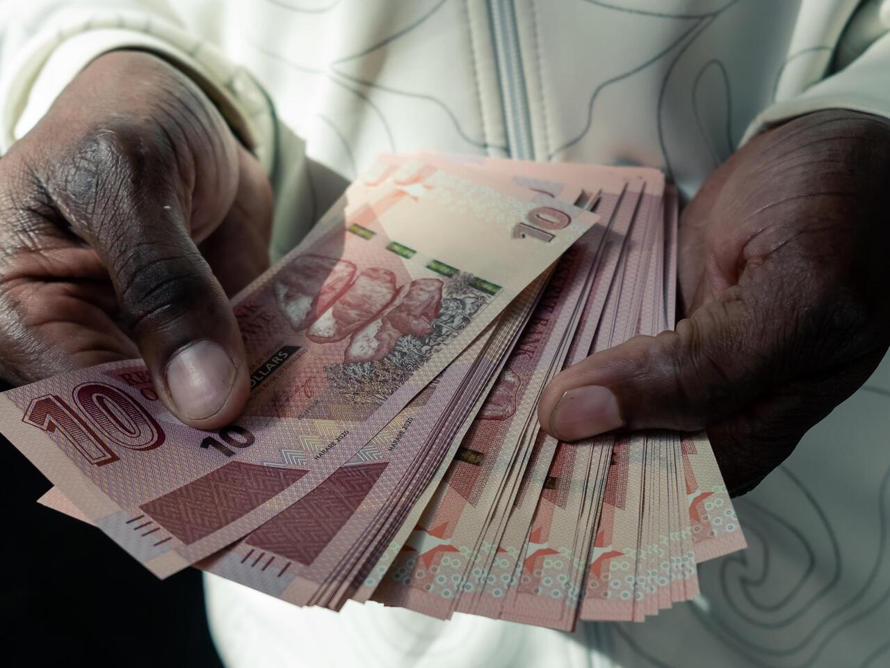 A man counts a wad of the new Zimbabwean ten-dollar notes received from an ATM outside a bank in Harare on May 20, 2020.